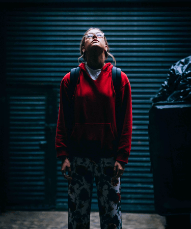 Girl standing alone in an alley looking up into the sky for the play Material Girls.