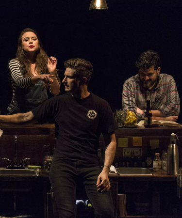 Three actors conversing onstage in a bar setting for the play [PORTO]