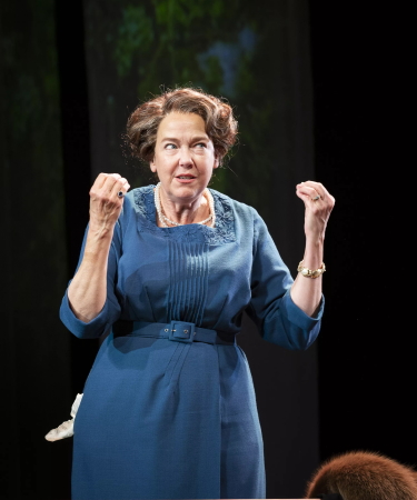 An middle-aged actress in a blue dress plays Eleanor Roosevelt while standing center stage in the TRW Plays production of "Eleanor".